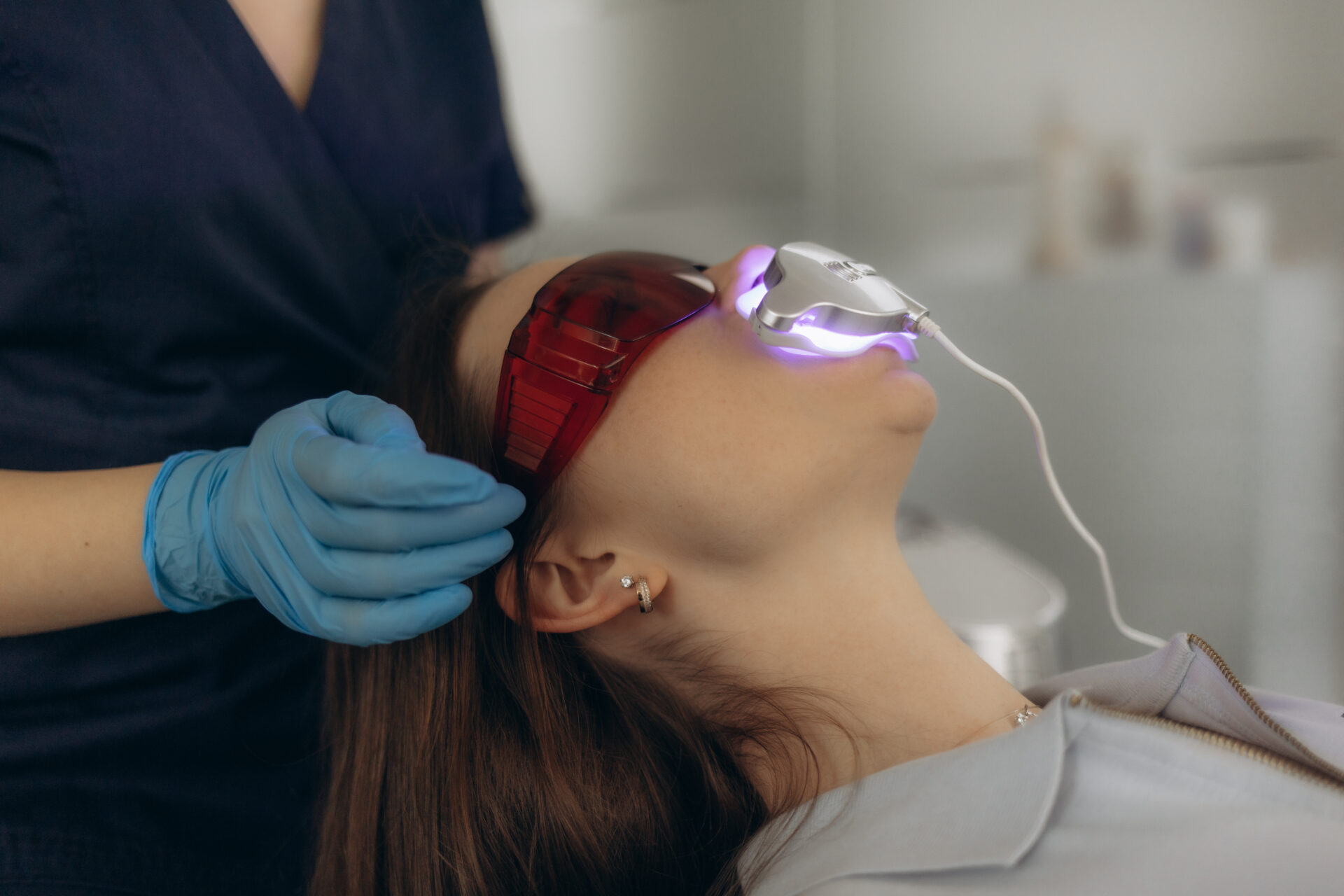Woman in tinted glasses under a whitening light in a dental chair