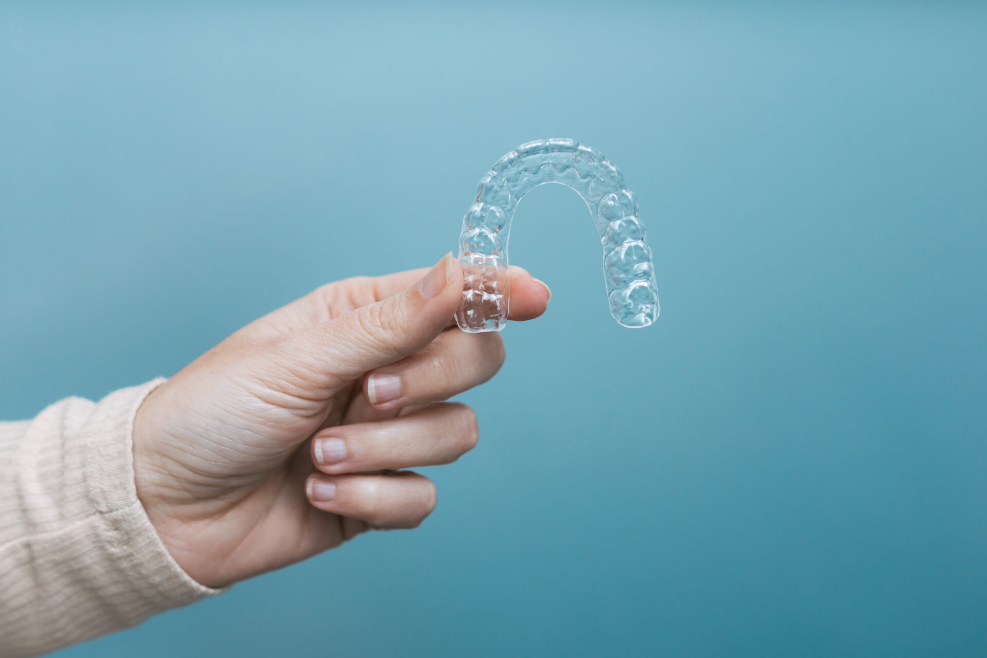 Hand holding a clear aligner against a teal background